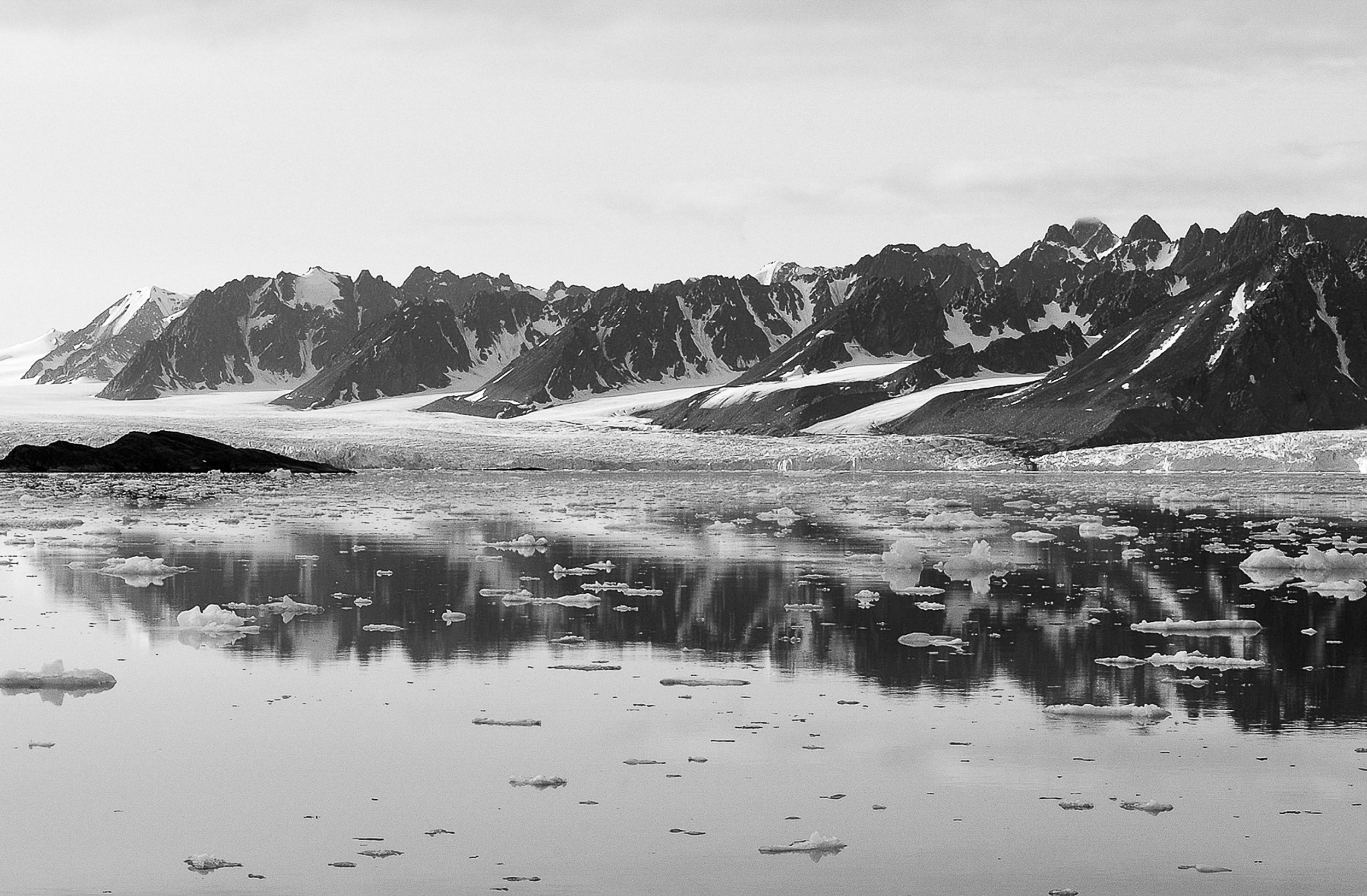 Photo de montagnes enneigées derrière un lac sur lequel flotte de la glace.