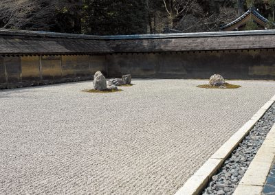 Quelques rocs granitiques au milieu d'un jardin zen en gravier ratissé entouré de haut murs.