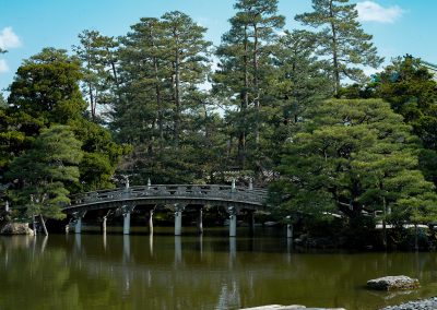 Un pont légèrement bombé enjambe un lac bordé d'arbres majestueux.