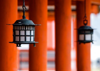 Des lanternes en fonte suspendues devant des piliers rouges évoquant un temple shinto.