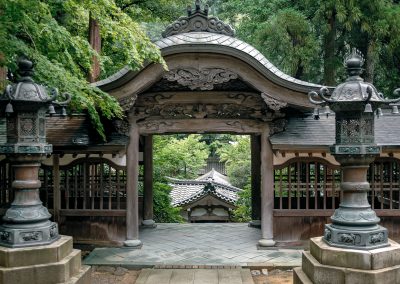 Au milieu d'une forêt verdoyante, un portique en bois travaillé mène à un temple en contre-bas.